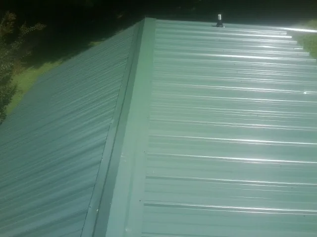 New green metal panels meeting at the ridge of a roof — Flat Roof Repair work by our crew in Longwood