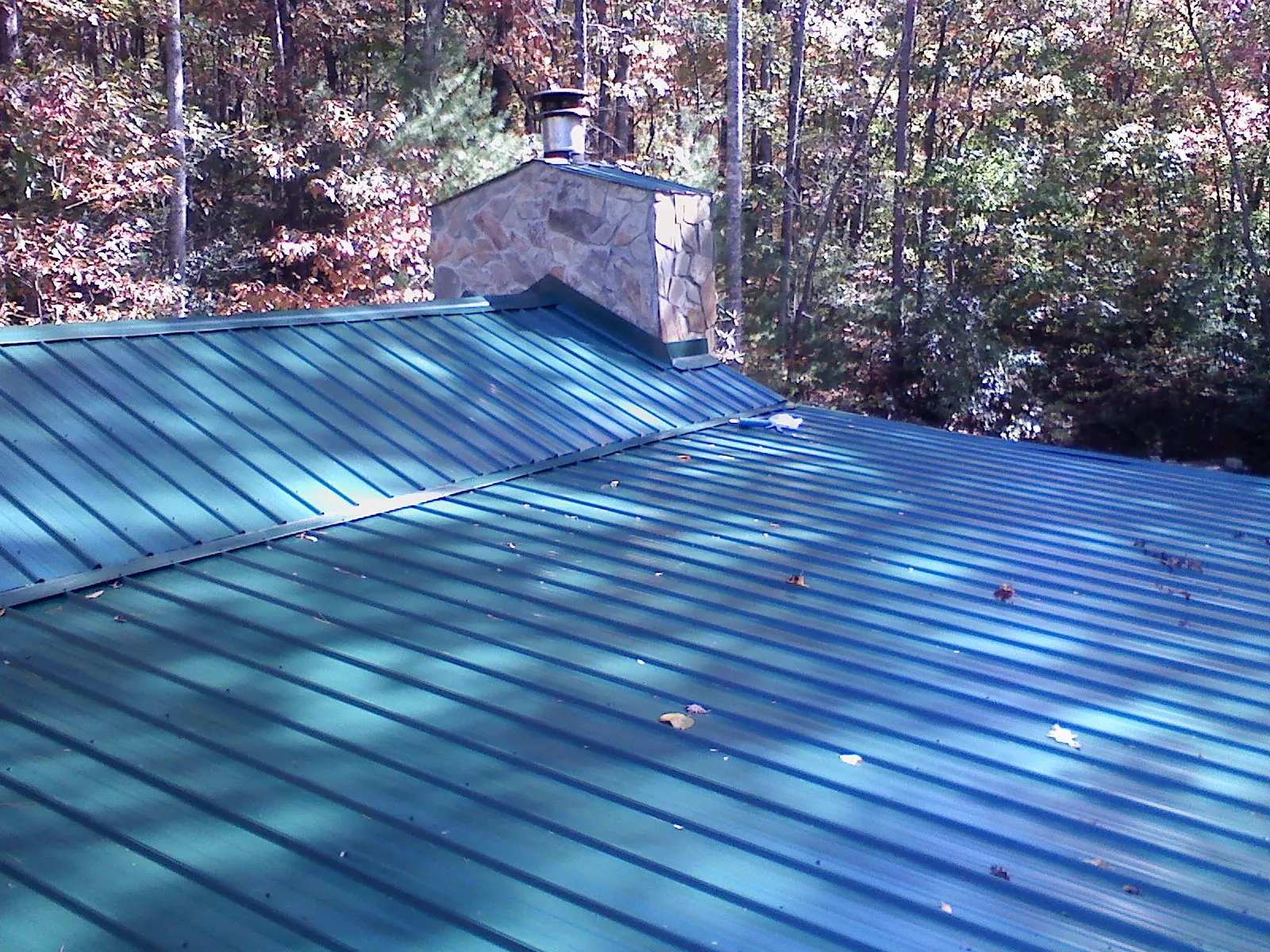 New green metal roof and stone chimney surrounded by autumn woods in Longwood