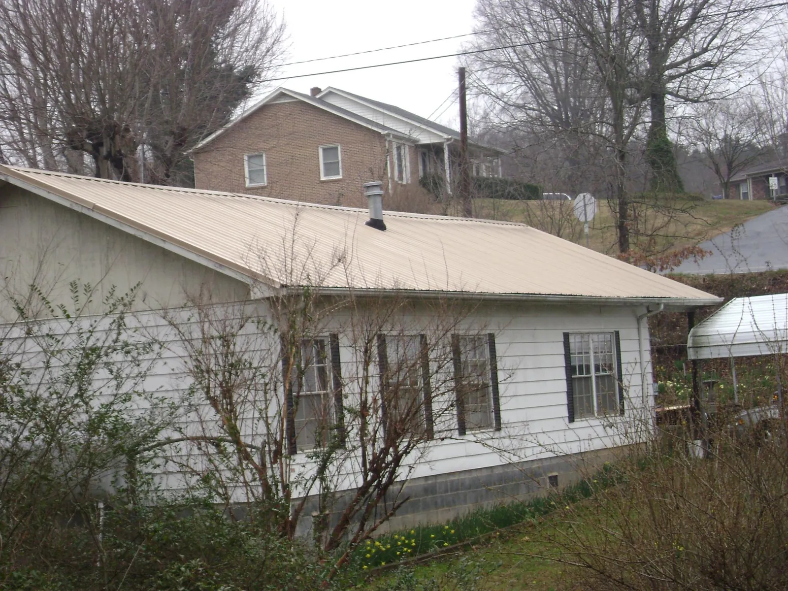 Tan metal roof on a white sided house set into a hillside — Commercial Roofing by Roofing Brothers in Longwood