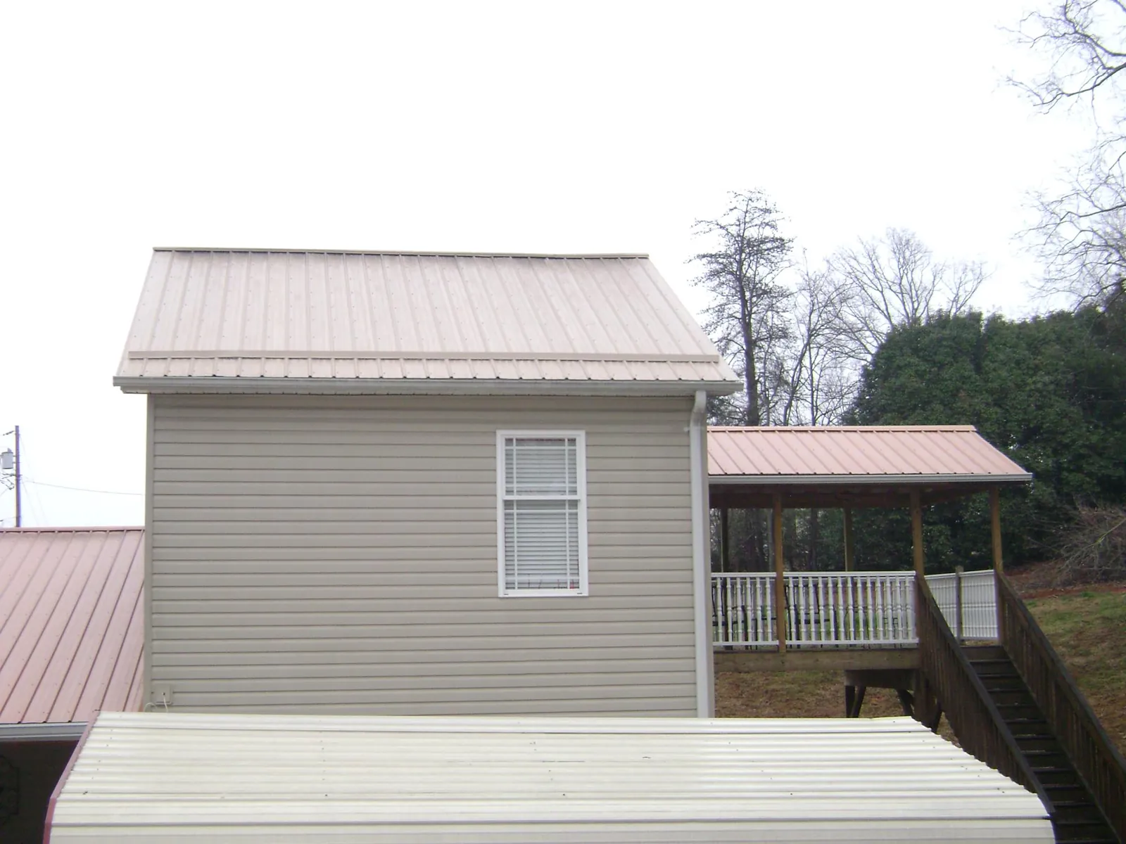Tan metal roofs on a two story addition and attached porch, from a Roof Replacement job in Longwood